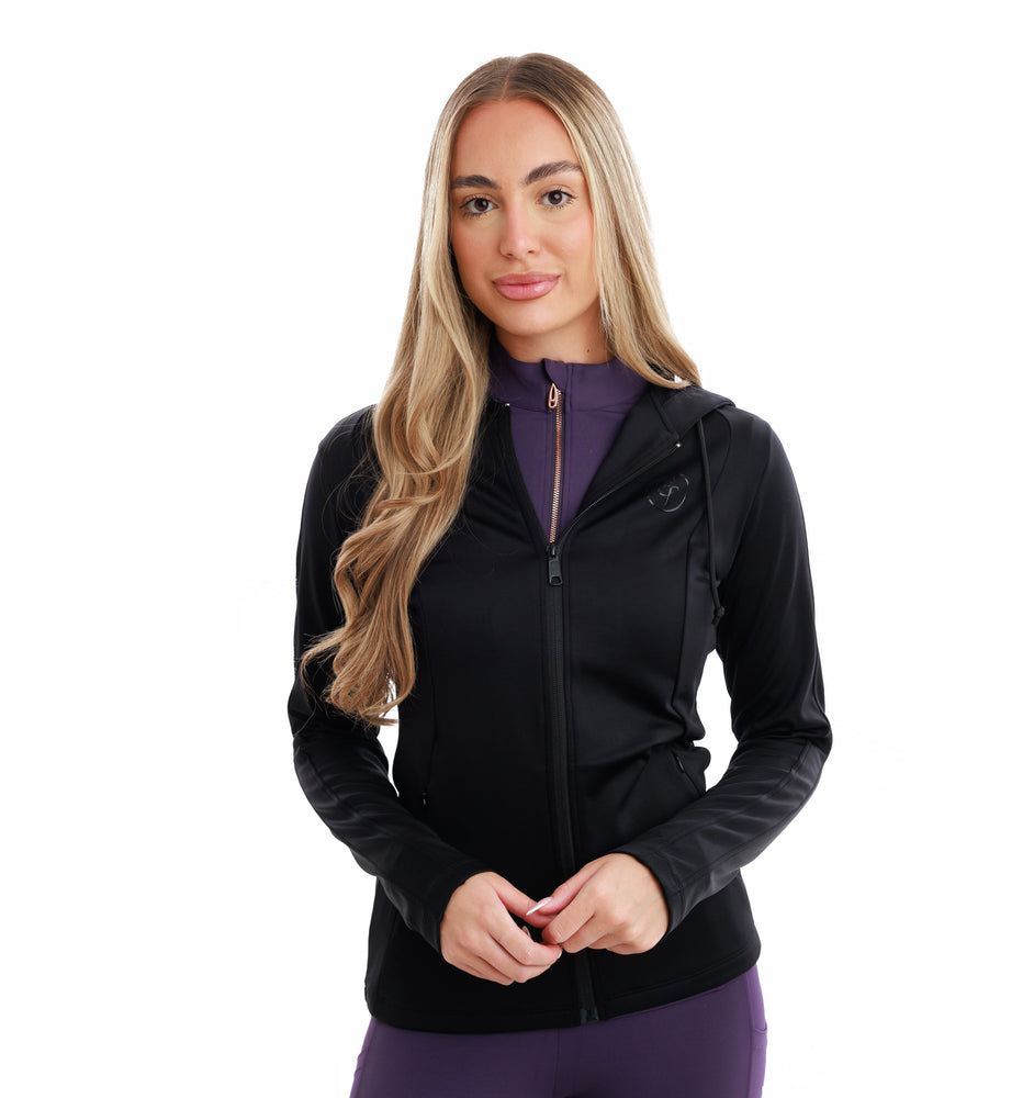
                  
                    Woman wearing a black equestrian jacket zipped up over purple outfit with a white background
                  
                