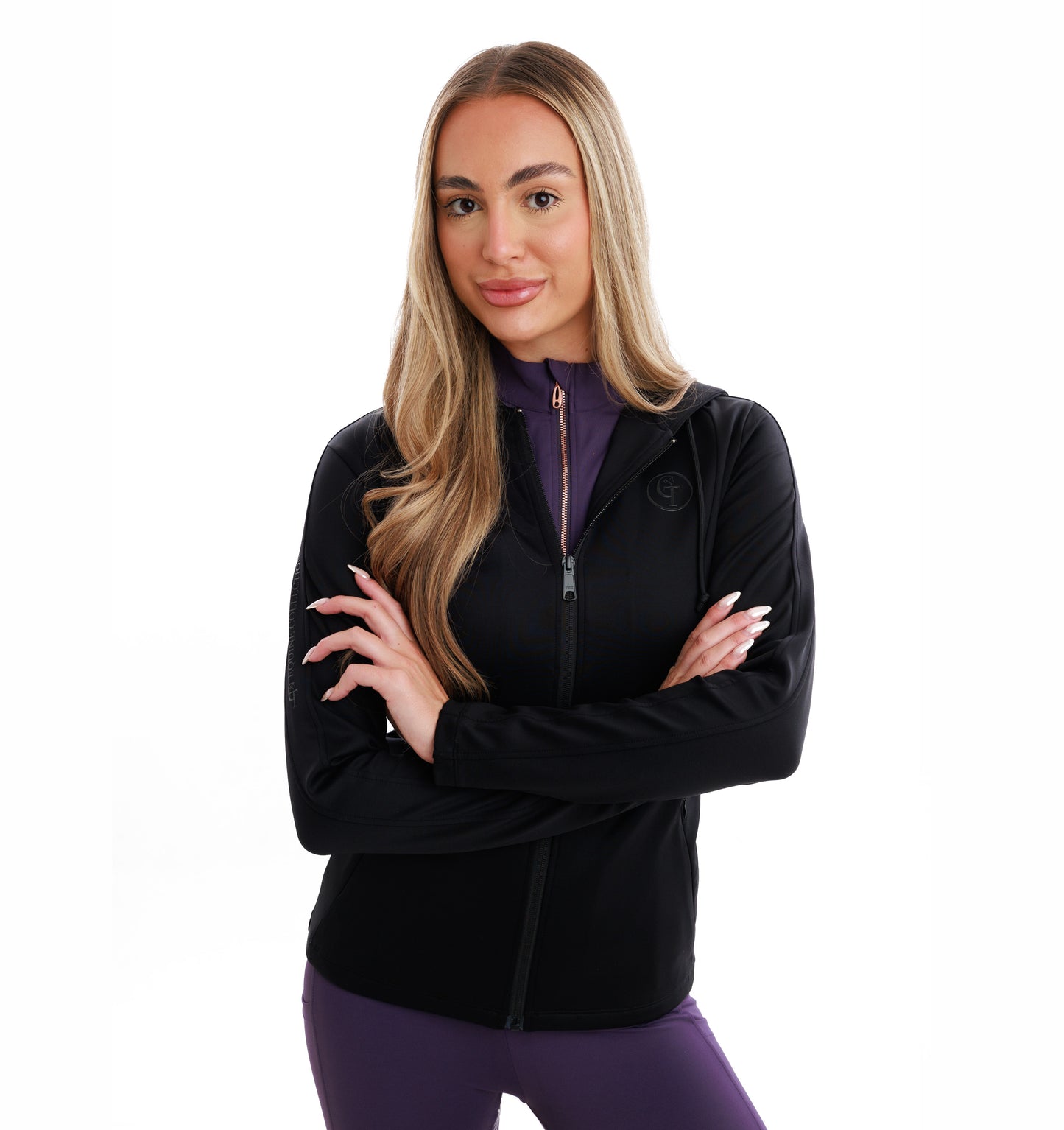 
                  
                    Woman wearing a black zip jacket over a full purple equestrian outfit with her arms crossed over her chest
                  
                