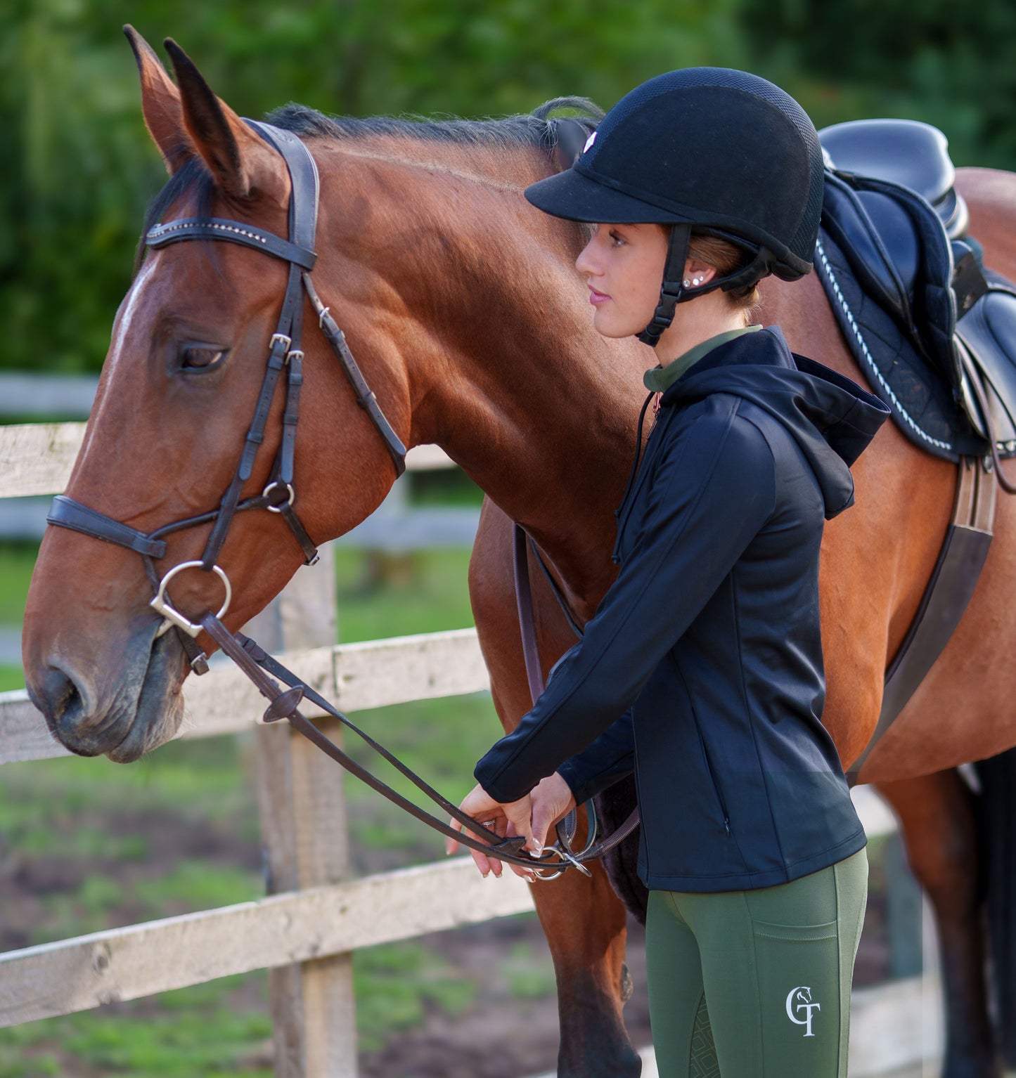 
                  
                    Person in full equestrian attire standing next to a brown horse in an outdoor setting
                  
                