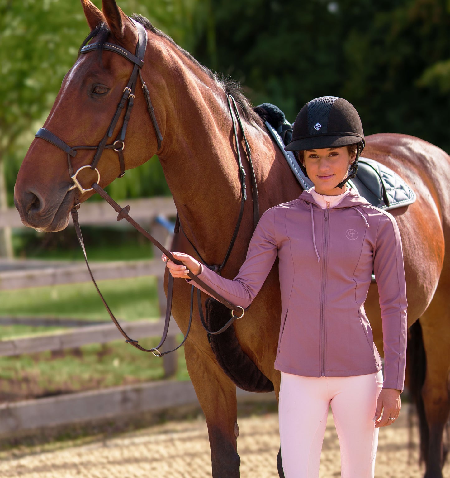 
                  
                    Woman in equestrian attire standing next to a brown horse in an outdoor setting
                  
                