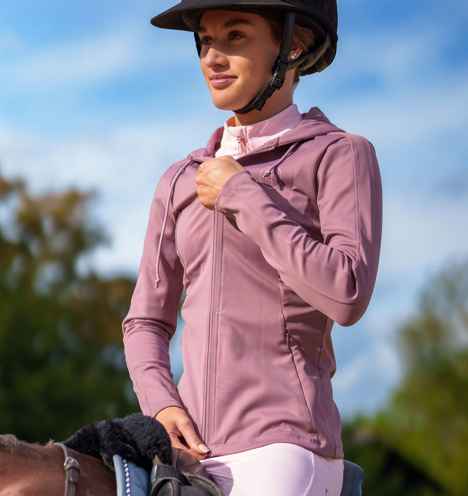 
                  
                    Woman in a pink equestrian jacket and helmet on a horse with a blurred natural background
                  
                