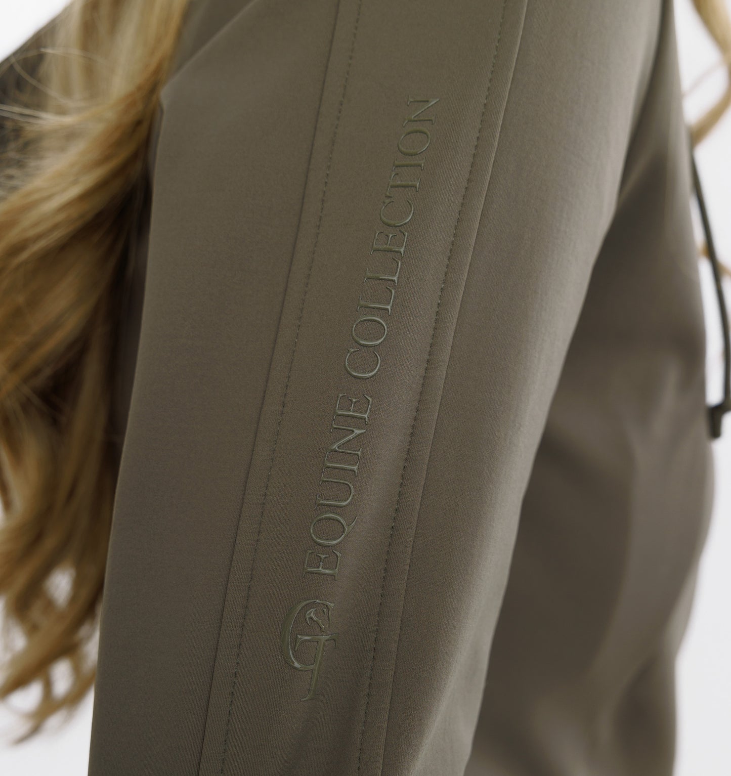 
                  
                    Close-up of a beige equestrian jacket with 'Equine Collection' branding.
                  
                