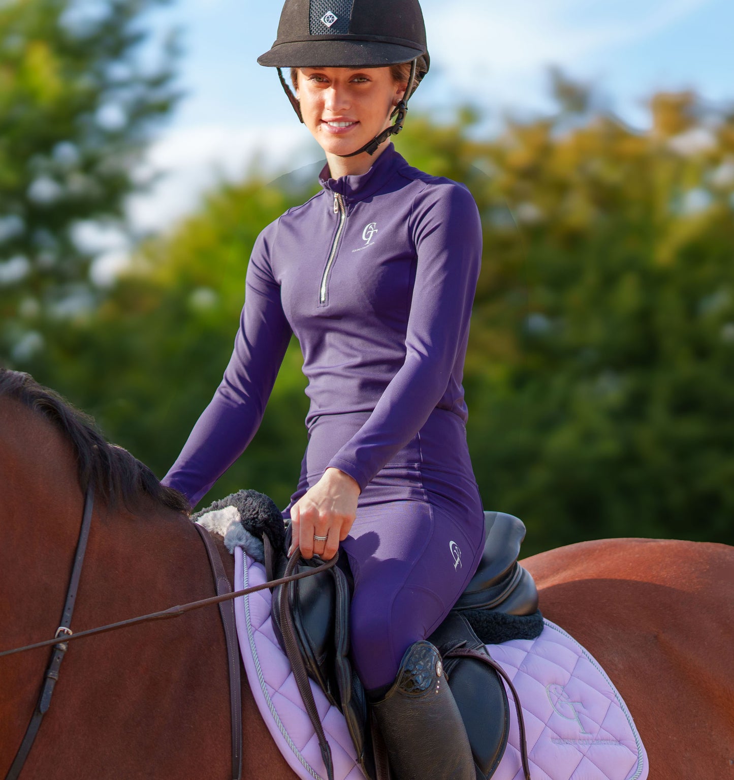 
                  
                    Woman in a purple equestrian outfit sitting on a horse with a blurred natural background
                  
                