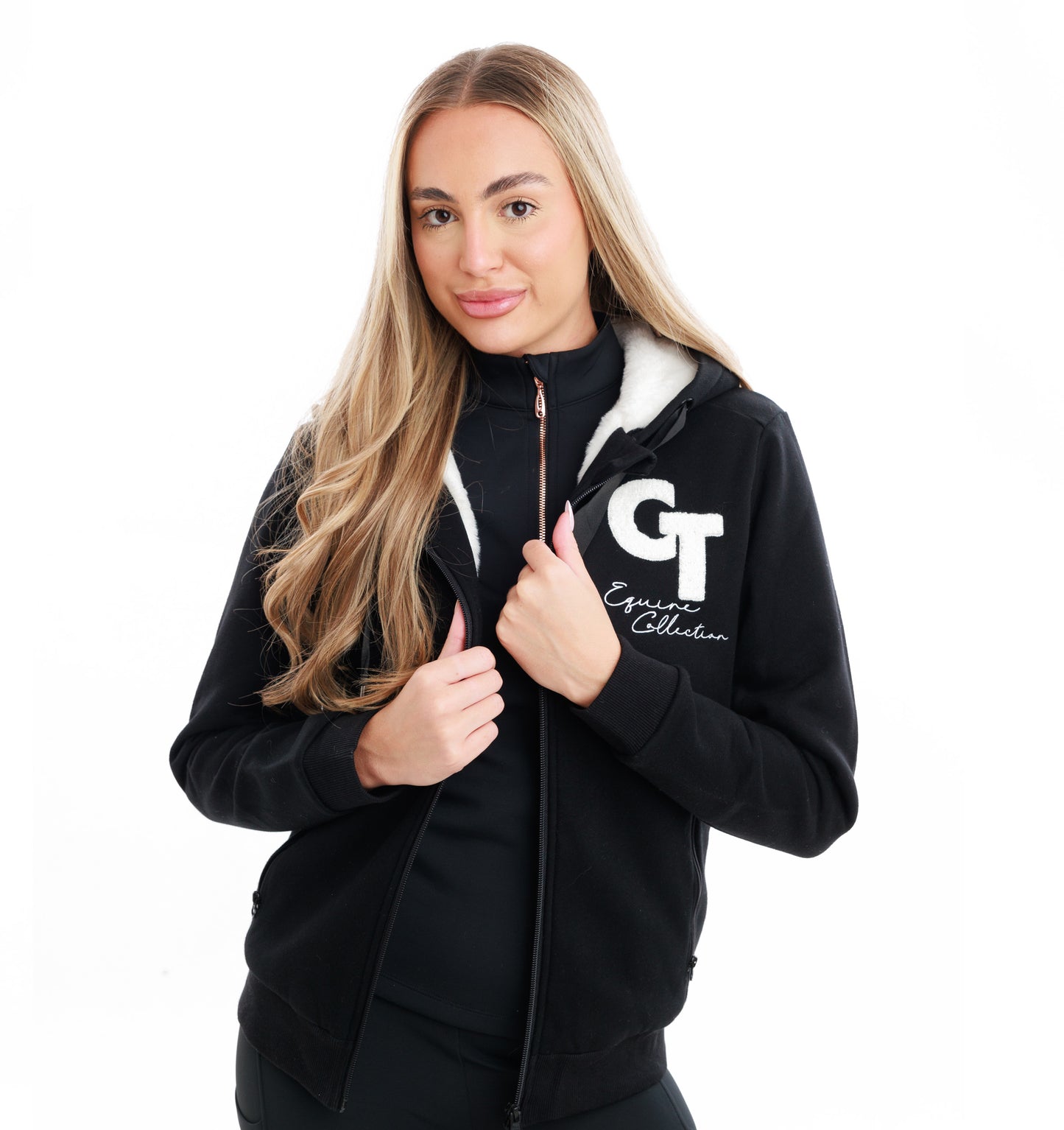 
                  
                    Woman wearing a black jacket over a black jumper, holding the front of the jacket with a logo on a white background
                  
                