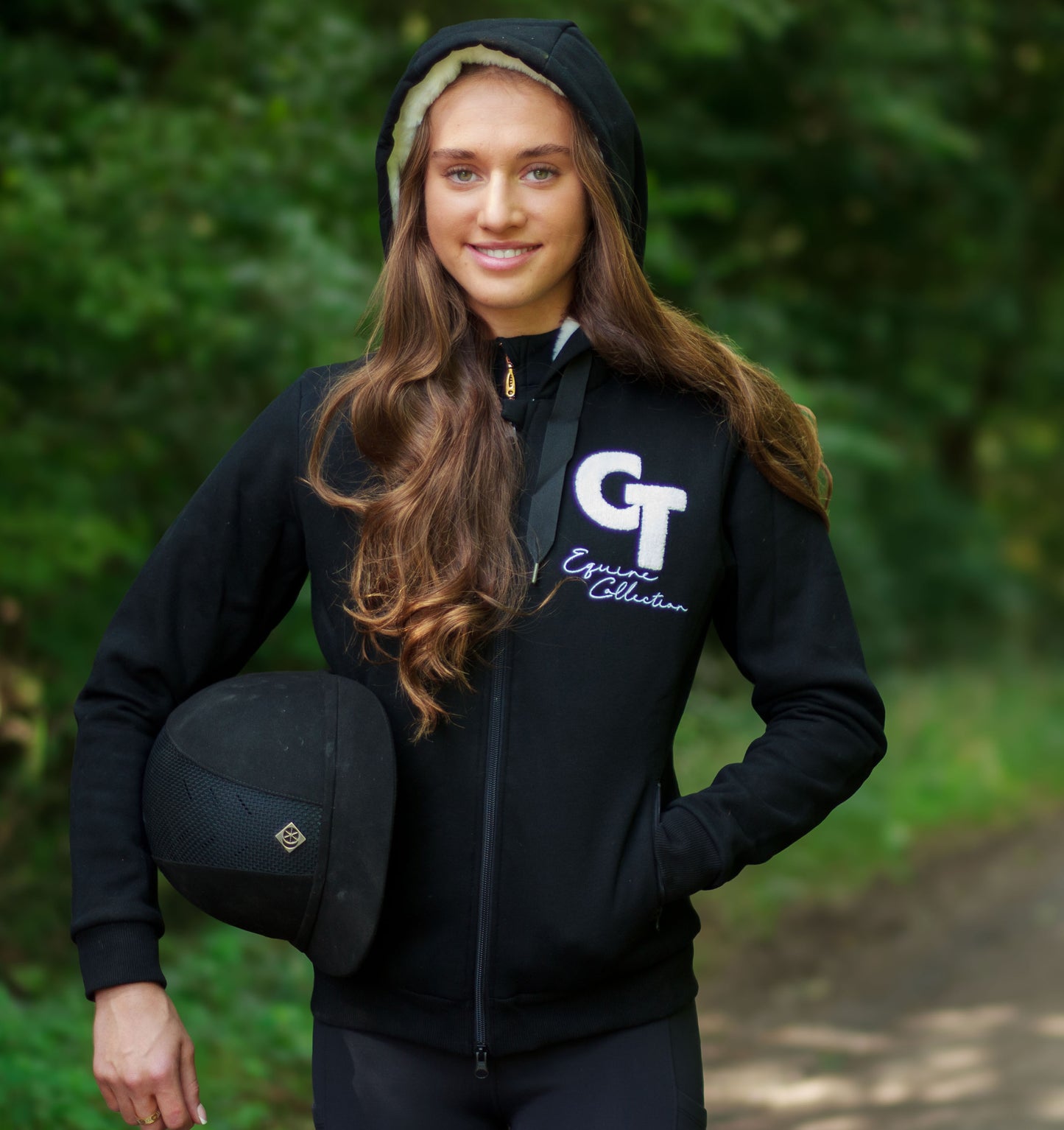 
                  
                    Person wearing a black hoodie with a logo, holding a helmet, outdoors.
                  
                