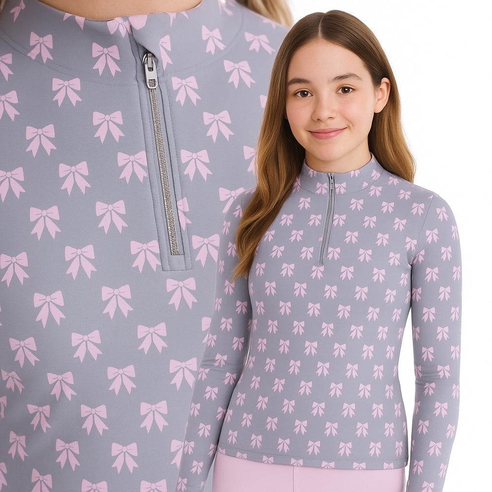 Image of a young girl wearing a blue long sleeve top with quarter zip and pink bows