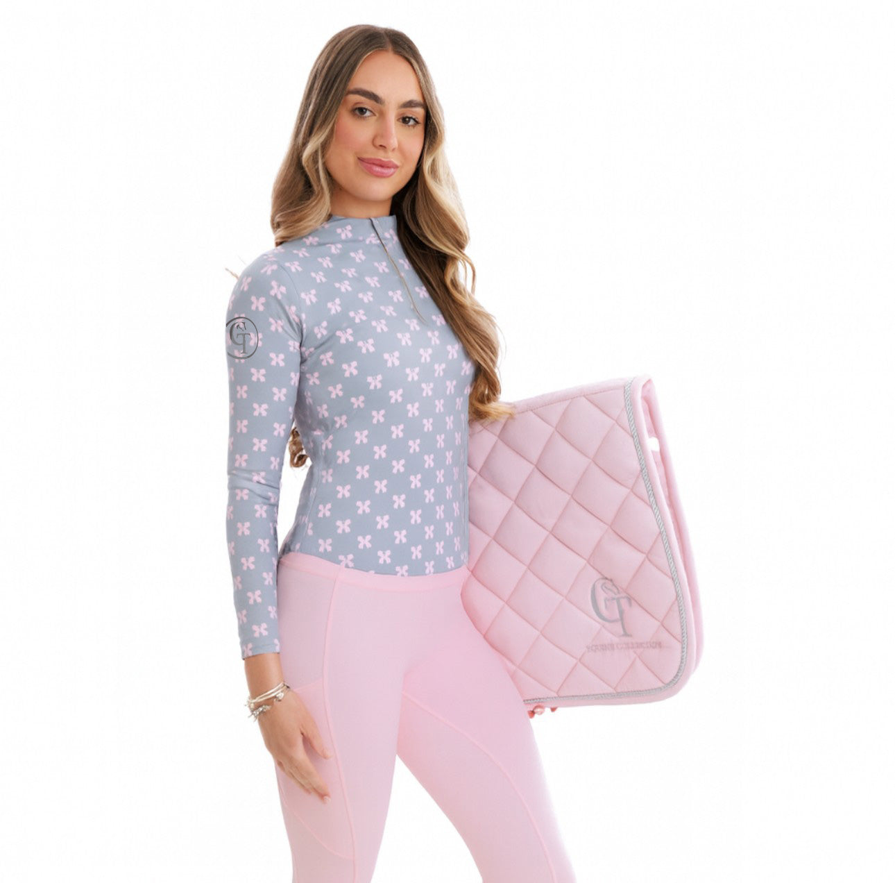 
                  
                    Woman holding a pink quilted saddle pad with a patterned shirt and pink trousers on a white background
                  
                